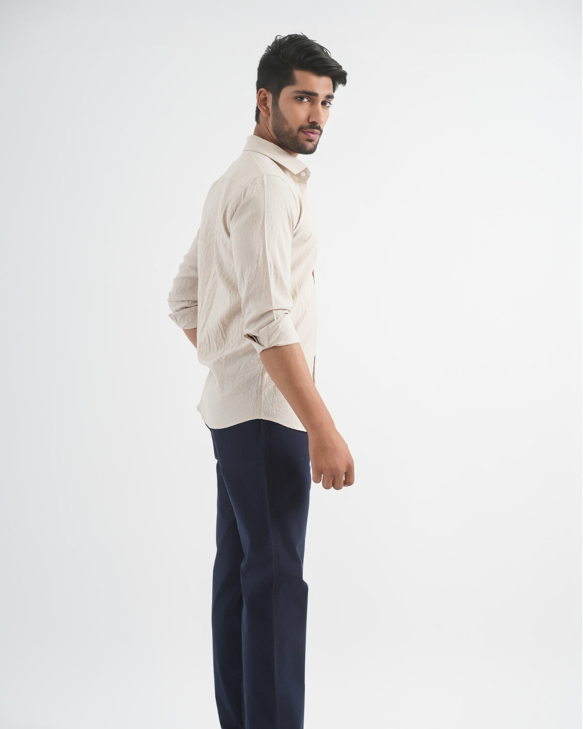 Man wearing a beige shirt and navy pants on a white background