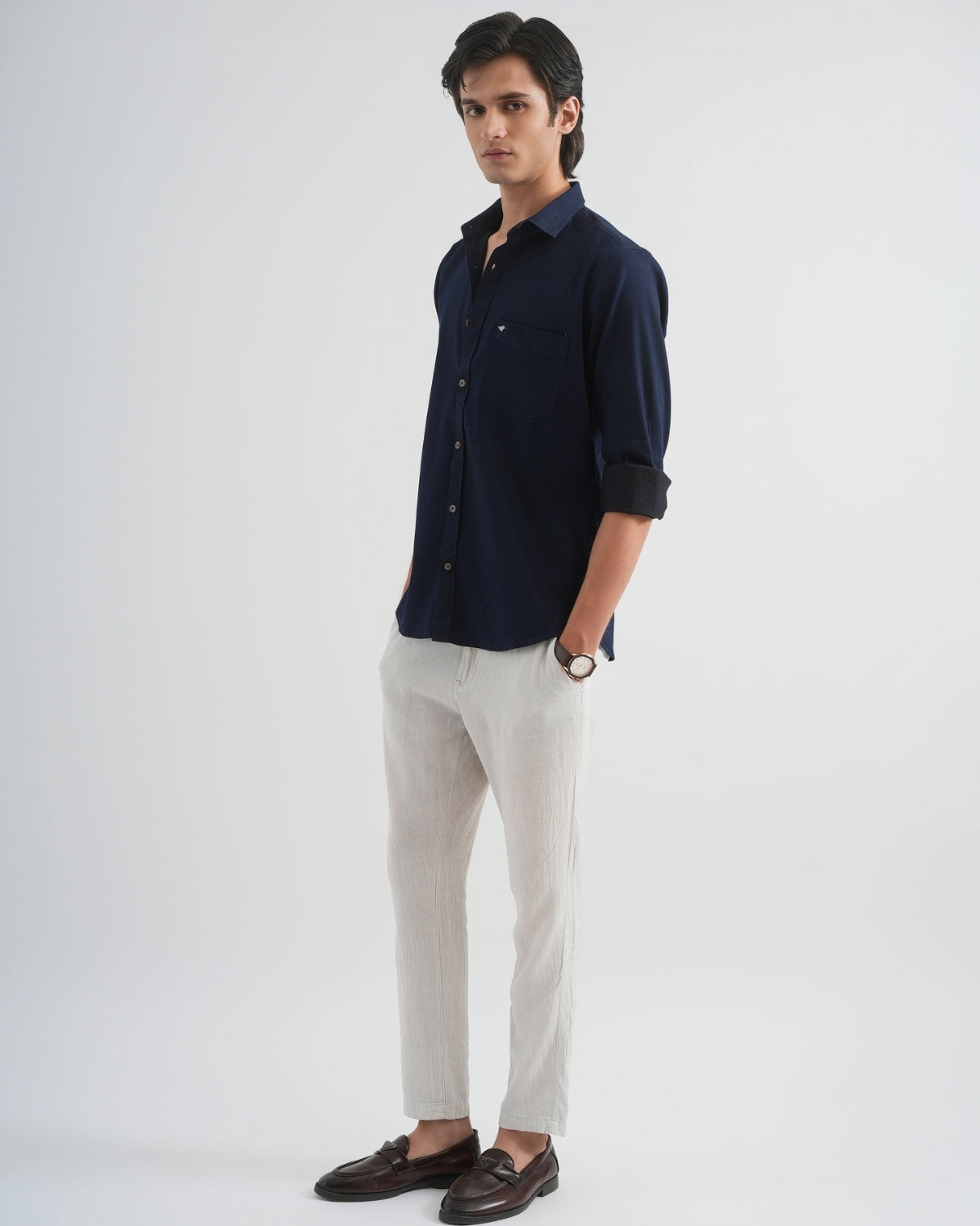 Man wearing a navy shirt, light gray pants, and brown shoes on a white background