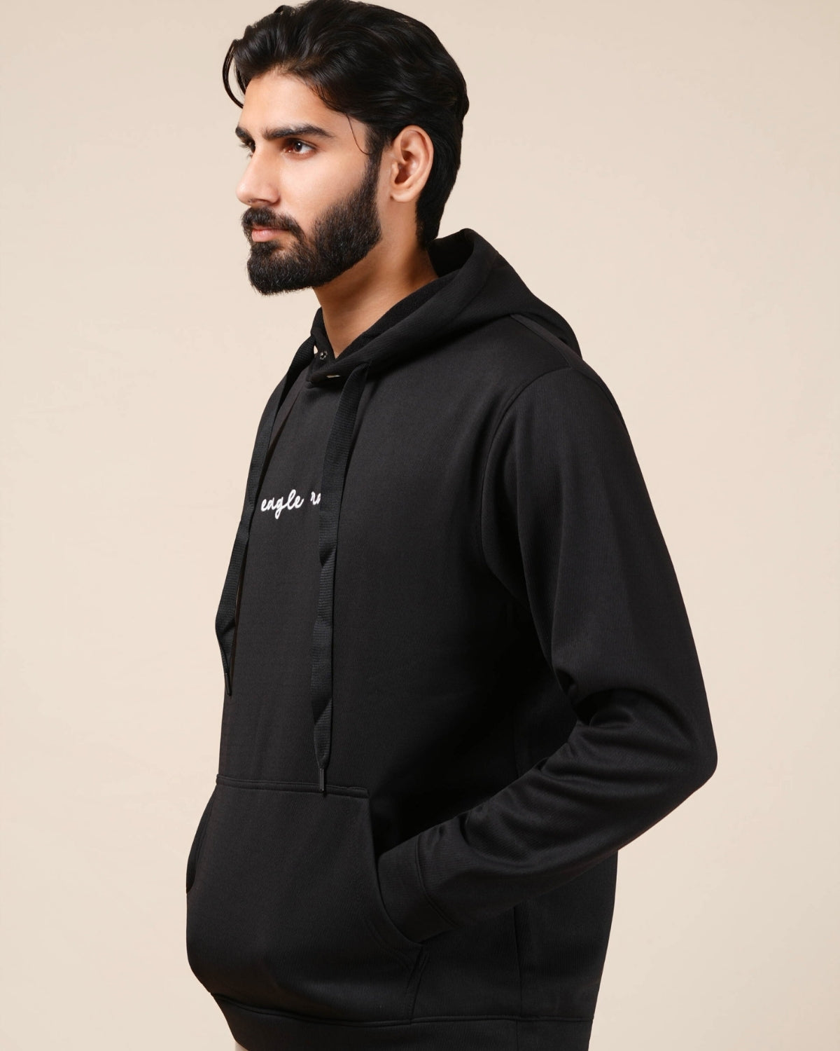 Man wearing a black hoodie with a logo on a beige background